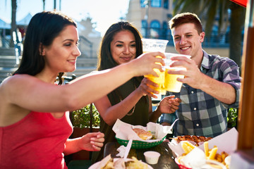 group of three friends making a toast with beer cups at lunch on summer day