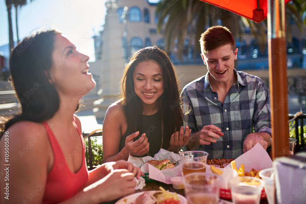 Wall mural group of friends having great time eating lunch together outside under summer sun