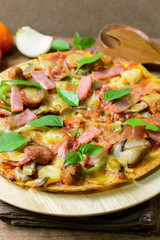 Rustic pizza with becon, salami, mozzarella and basil