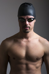 Portrait of a young man with swimming goggles on gray background