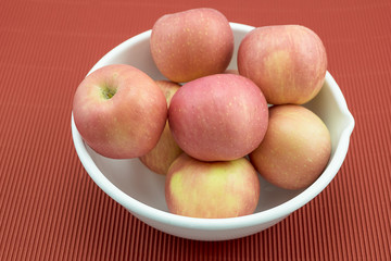 Apples in a white bowl, isolated on red background