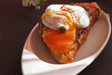 Breakfast of croissants with salmon, poached egg on a white plate