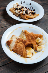 pancakes with chocolate and banana on a wooden background