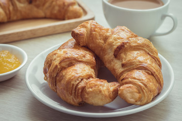Fresh croissants on plate with jam and coffee cup
