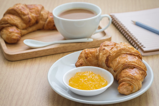 Croissant with jam on plate and coffee cup, book