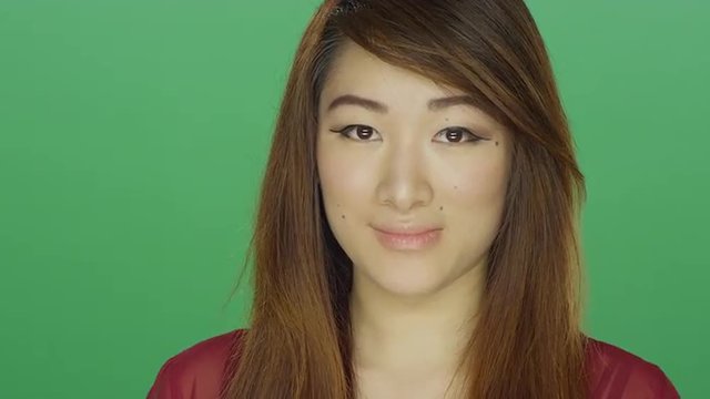 Young Asian woman awkwardly smiling, on a green screen studio background 