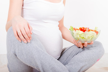 Beautiful young pregnant woman / teenager in white cloth eating healthy fresh salad with vegetebles