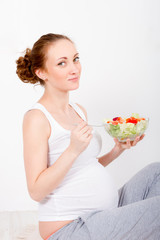 Beautiful young pregnant woman / teenager in white cloth eating healthy fresh salad with vegetebles