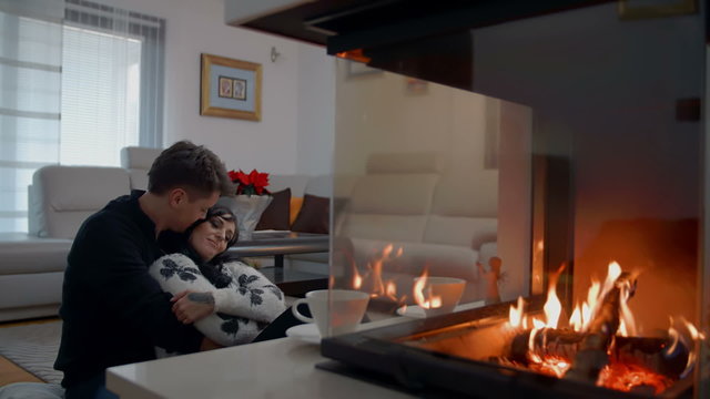 Young couple is cudding in front of the fire-place in their living room