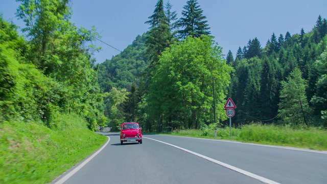 Small red vintage car driving on a main road