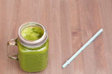 A green smoothie in a mason jar with tube on wooden background