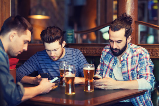male friends with smartphones drinking beer at bar