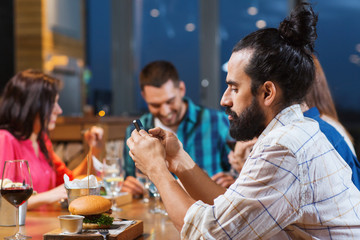 man with smartphone and friends at restaurant