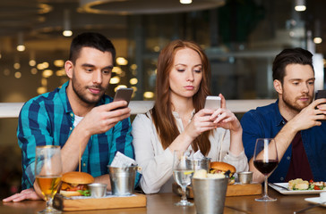 friends with smartphones dining at restaurant