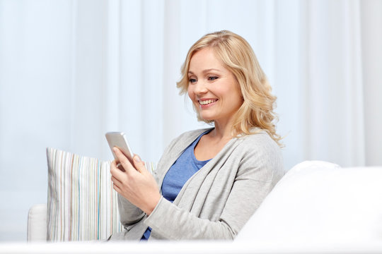 smiling woman with smartphone texting at home