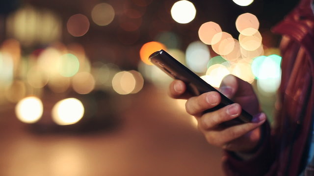 Man sms texting using app on smart phone at night in city. Close up