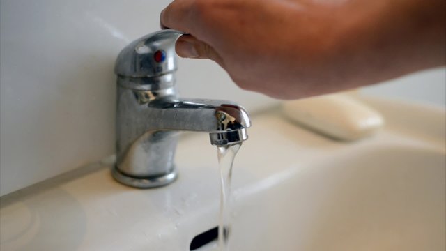 Mann &ouml;ffnet einen Wasserhahn beim Waschbecken