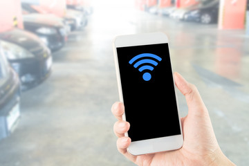 smartphone in hand with wi-fi icon on blurred car parking area