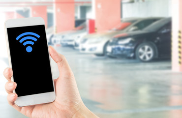 smartphone in hand with wi-fi icon on blurred car parking area