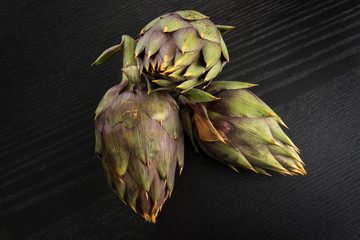 Obraz premium Tre carciofi freschi appoggiati sul tavolo di legno 