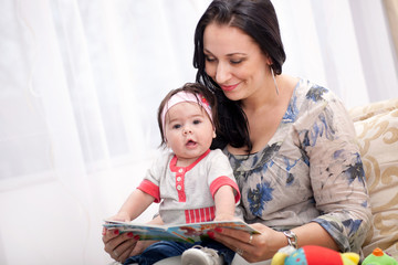 mother showing images in a book to her cute little daughter at h