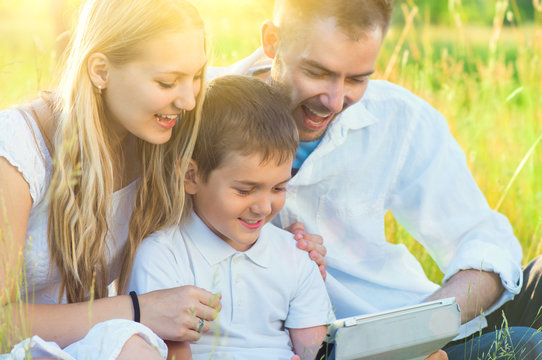 Happy young family with kid using tablet pc in summer park