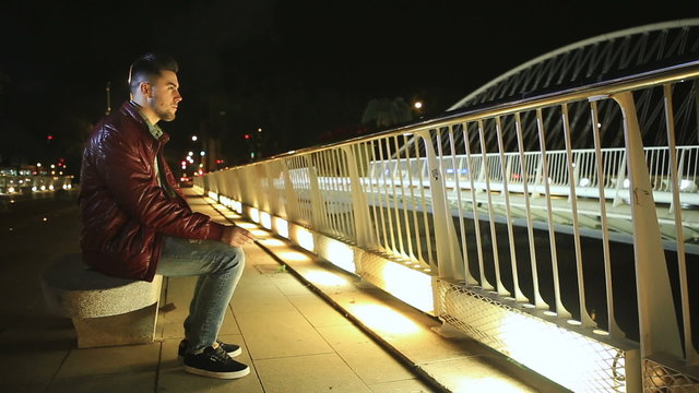 Young man smoking cigarette on a bridge at the night