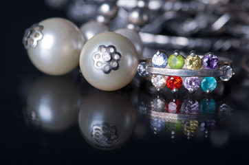 Silver jewelry on black background. Ring with colored stones. Earrings with pearls. Jewelry creates a mirror image.