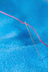 Macro red thread through needle hole on blue blurred background