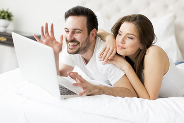 Fototapeta premium Young couple with laptop in the bed