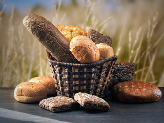 Many mixed breads and buns in a basket on the table. Background - nature, ear of wheat, oats, blue sky 