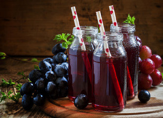 Jus de raisin noir dans des bouteilles en verre avec pailles, raisins bleus, noir