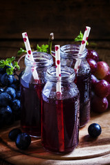 Dark grape juice in glass bottles with straws, blue grapes, dark