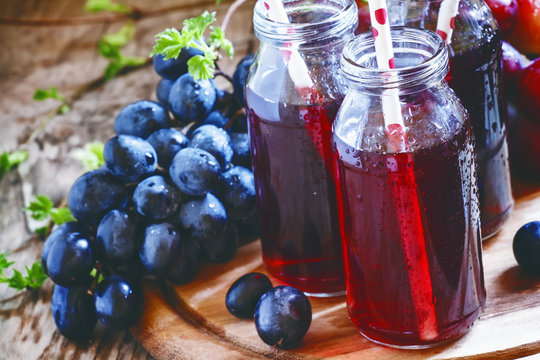 Dark grape juice in glass bottles with straws, blue grapes, dark