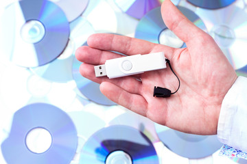 Man's hand with pendrive over CD's background. Concept of data s