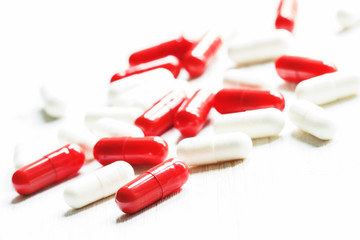 Red and white tablets in capsules on a white wooden background,