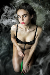 Sexy young brunette woman in black underwear smoking hookah with weathered brick wall on background