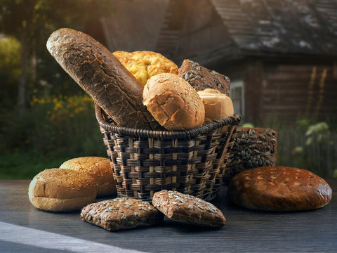 Many mixed breads and buns in a basket on the table. Background - village houses. Village