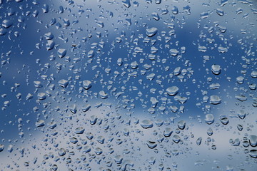 Rain drops on window with blue cloudy sky in background