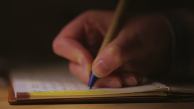 A woman writing into notebook , sitting by a lamp. Closeup.