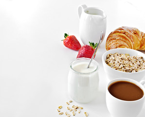 Breakfast with coffee, yogurt, oatmeal, croissant and strawberry.
