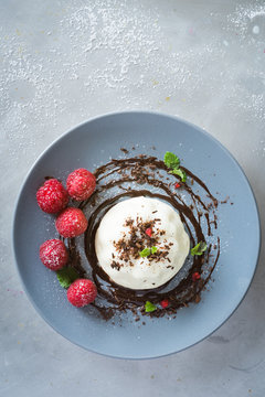 Beautifully plated vanilla panna cotta with chocolate sauce and fresh raspberries on metal countertop. Selective focus.