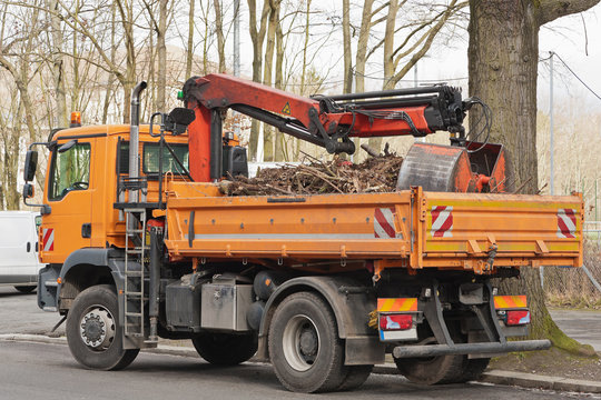 Ein oranger LKW mit Ladekran und Greifer gefüllt mit Baumschnitt