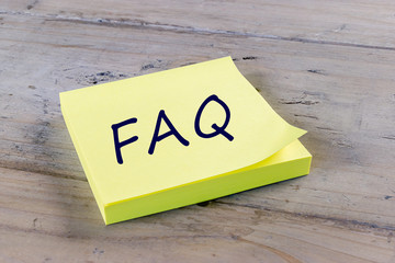 FAQ Frequently Asked Questions on yellow post it note.
Wood background.