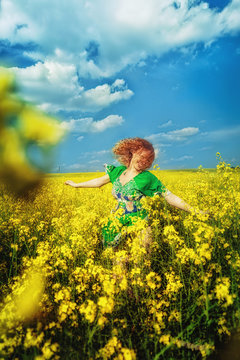 Happy red-haired young girl in a green dress jumping in yellow field