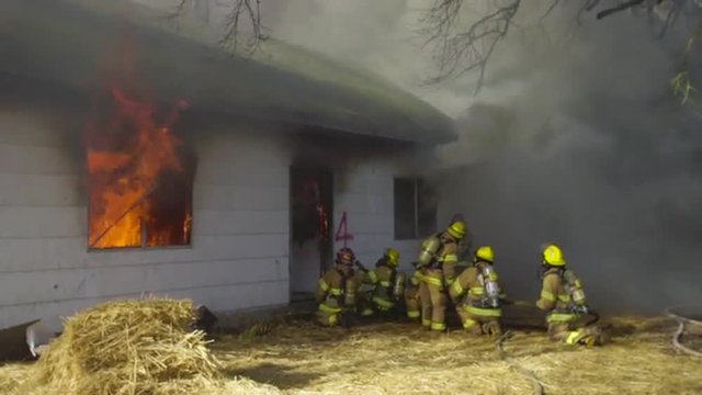 Firefighters battle a buring house through think smoke 