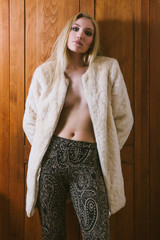 Young beautiful blonde sexy girl in wool coat and colorful pants standing in front of old locker,...
