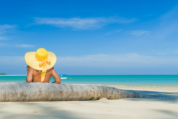 Fototapeta na wymiar Woman in bikini wearing a yellow hat at tropical beach