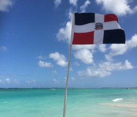 Dominican Republic flag waiving in the wind by the caribean ocean and beach