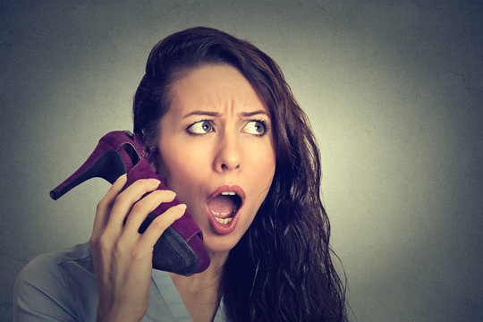 woman looking excited, surprised holding high heeled shoe in her hand as phone